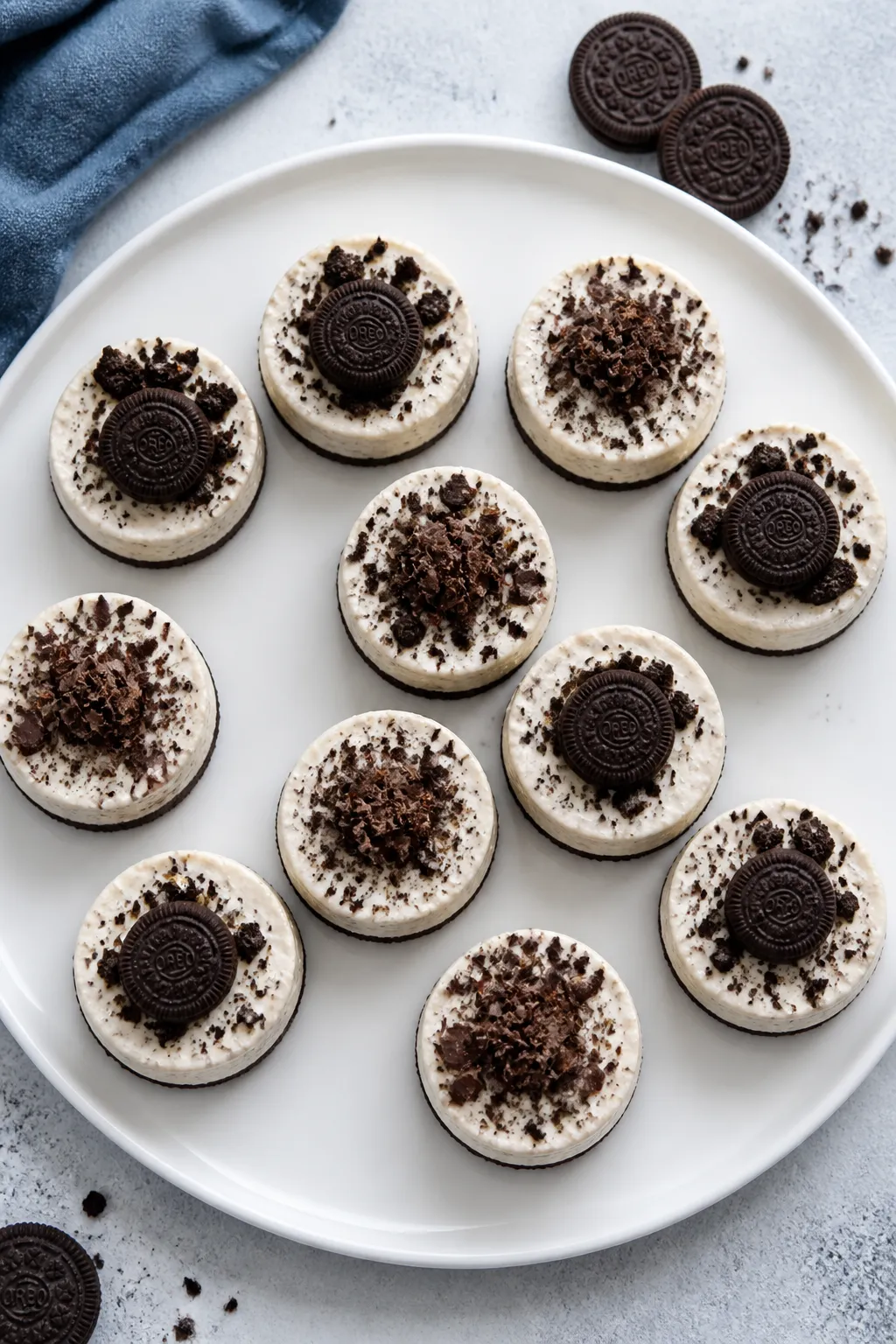 Final plated overhead: Finished no bake mini Oreo cheesecakes on a matte white platter, paper liners